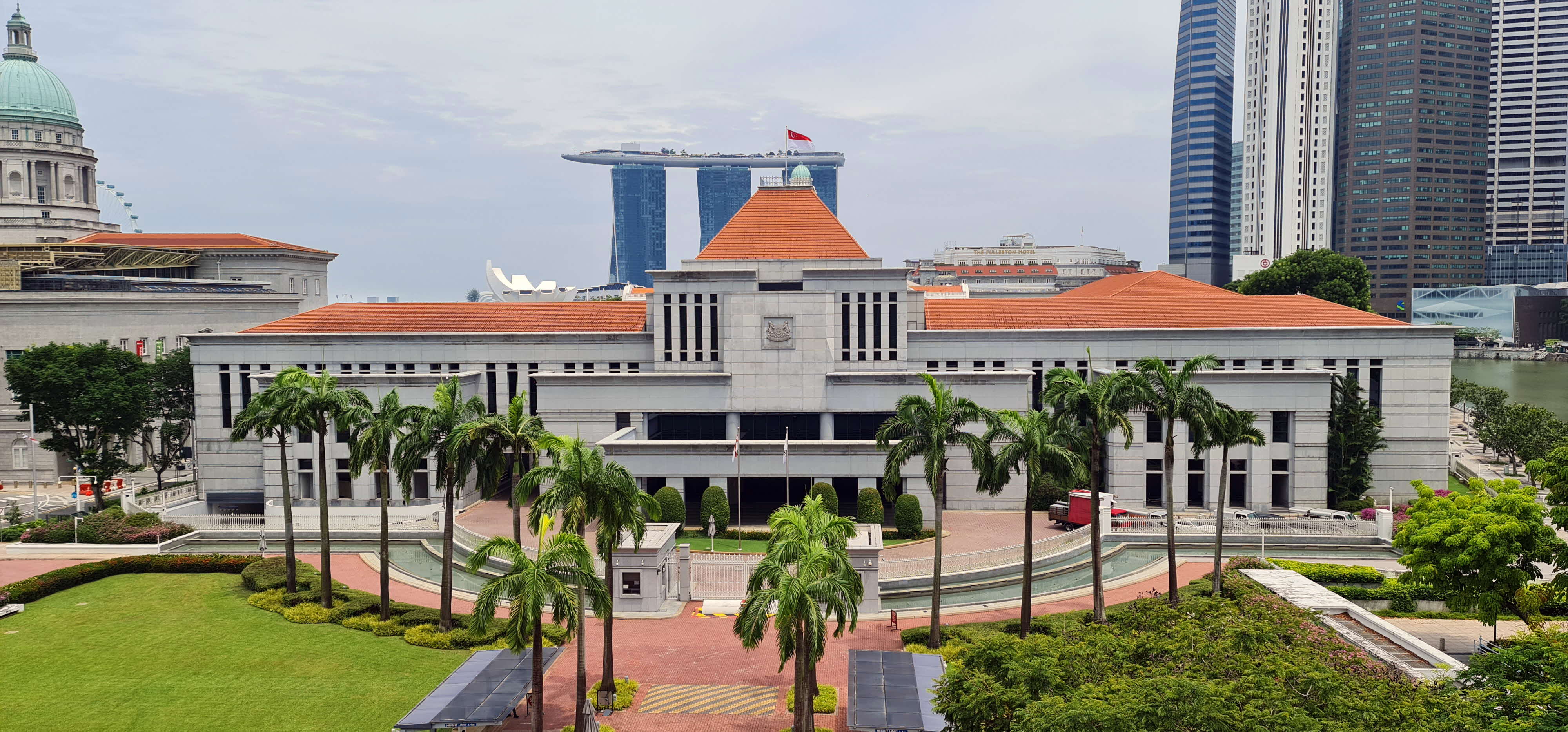 A large building with red rooftops, green palm trees, and a futuristic structure in the background.